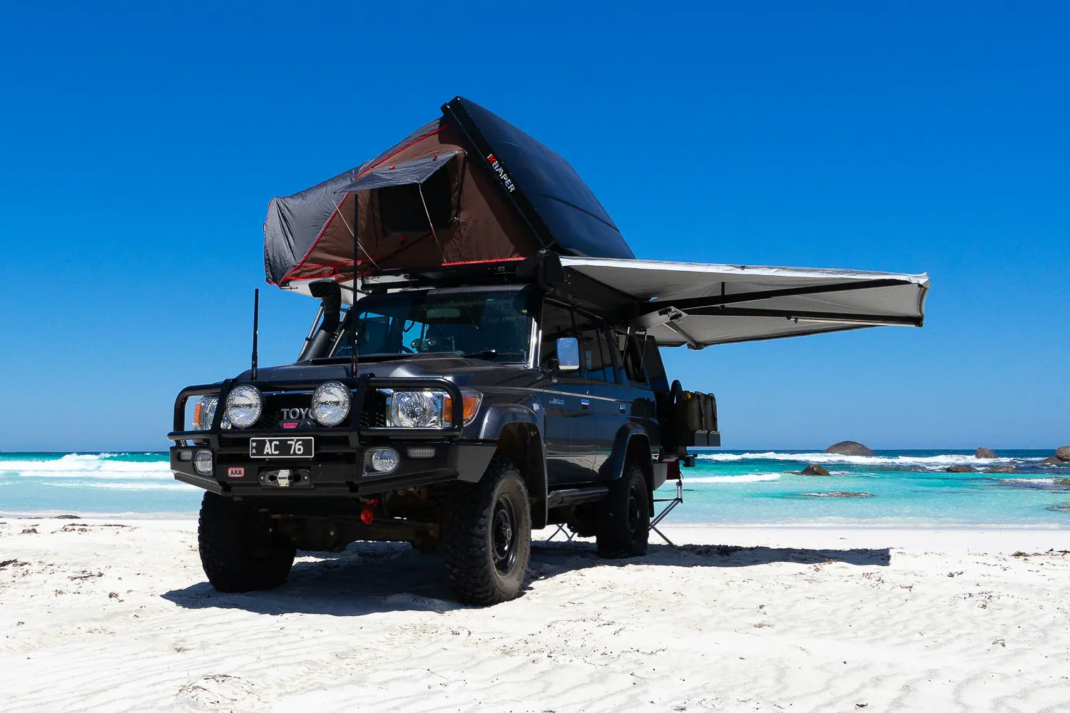 An offroad vehicle with a hard shell tent and 270 degree awning on a beach